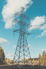 Supports high-voltage power lines against the blue sky with clouds. Electrical industry.