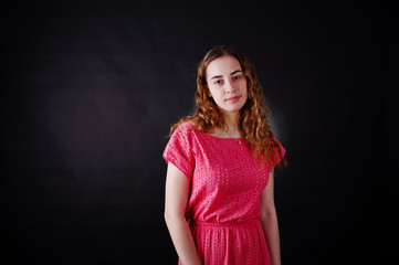 Fototapeta premium Young girl in red dress against black background on studio.