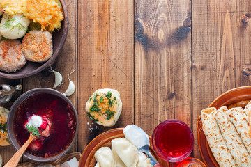 Traditional dishes in Ukrainian cuisine on a wooden table - borsch, vareniki, pampushki with garlic, lard, pancakes, potatoes, vvar, top view, horizontal, copy space