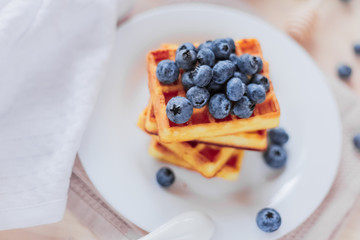Belgian waffles with blueberries on the light wooden table. Healthy breakfast. 