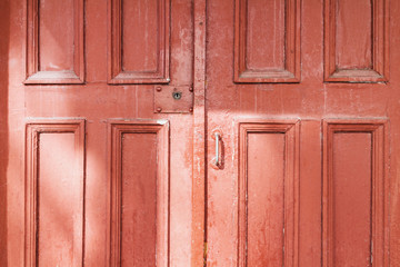 Old red wooden doors on the street with sunlight reflections. Closeup