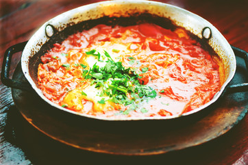 Shakshuka. Traditional jewish food and middle eastern cuisine recipe. Fried eggs, tomatoes, bell pepper and parsley in a pan. Close up, selective focus. Toned effect