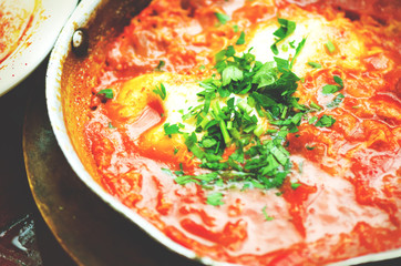 Shakshuka. Traditional jewish food and middle eastern cuisine recipe. Fried eggs, tomatoes, bell pepper and parsley in a pan. Close up, selective focus. Toned effect