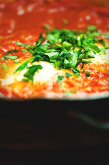 Shakshuka. Traditional jewish food and middle eastern cuisine recipe. Fried eggs, tomatoes, bell pepper and parsley in a pan. Close up, selective focus. Toned effect