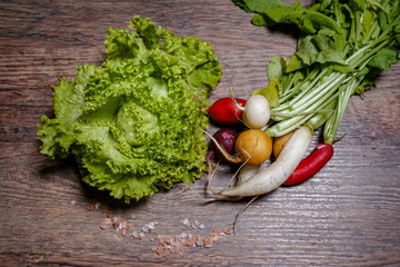 Fresh home-made green lettuce and colorful radishes on a wooden background. Detached from the home garden.