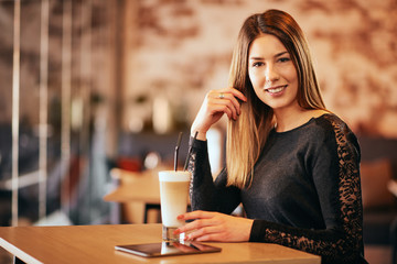 Young caucasian woman using tablet while sitting in cafe and drinking coffee.