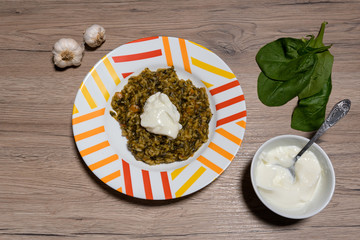 Delicious homemade risotto with spinach, onion and carrots. Decorated with yoghurt and garlic. On a wooden background.