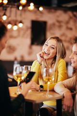 Girlfriends drinking wine and chatting while sitting in the bar.