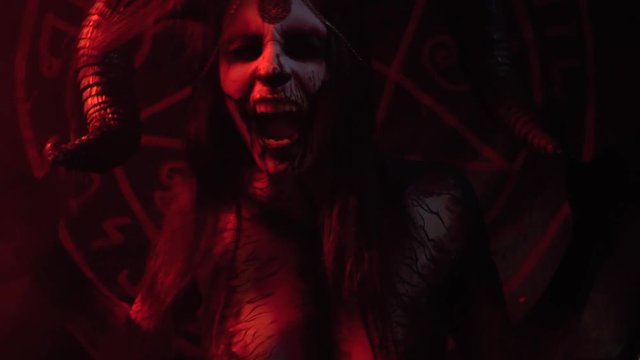 Satan with large horns performs a ritual and reads spells, body painting