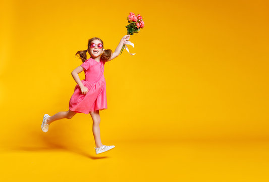 funny child girl runs and jumps with bouquet of flowers on colored background.