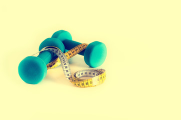 Fitness concept. Turquoise dumbbells and yellow measuring tape. Copyspace