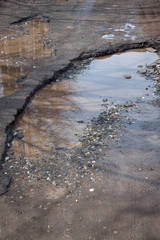 The bad asphalted road. Big pothole filled with water. Dangerous destroyed roadbed.