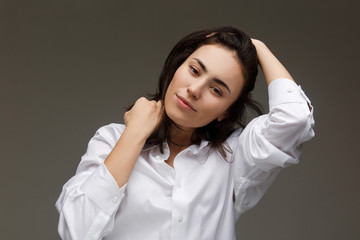 Beautiful girl in a white shirt embraces herself. On a light background.