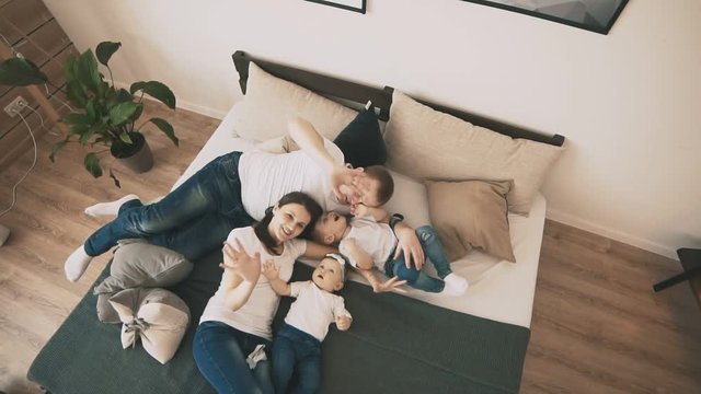 Cute family playing on bed at home in bedroom in slow motion. Happy family concept. Young family have fun indoor. Top view