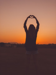 Girl holding heart shape in the sunset / sunrise time.