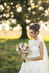 Beautiful bride with bouquet standing in the middle of field in the background of big tree