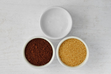 Homemade face scrub made out of coconut oil, coffee powder and brown sugar on wooden background