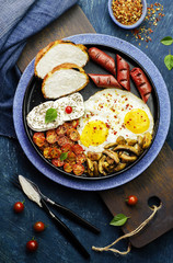Delicious breakfast with fried eggs,garlic baked cherry tomatoes,slices of cheese,sausage, crispy bread and mushroom.Top view with close -up.