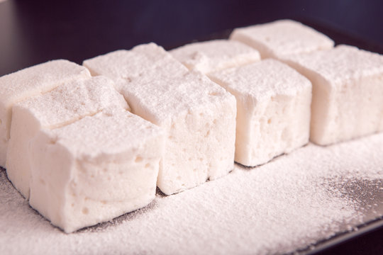 Marshmallow cubes sugar powdered lying on black plate