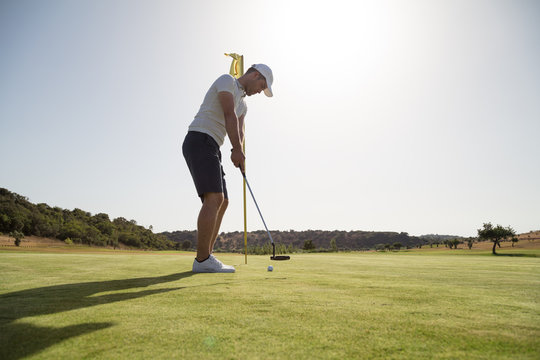 Young golfer putting golf ball in the hole