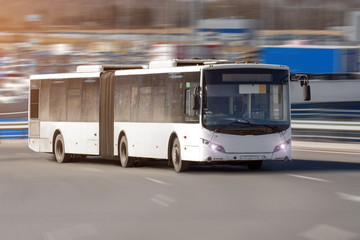 Passenger lengthened articulated bus city bus of white color rides at high speed along the highway.