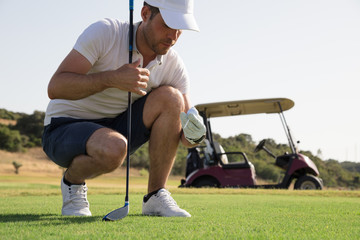 Golf player putting ball on the course before teeing off in front of golf cart