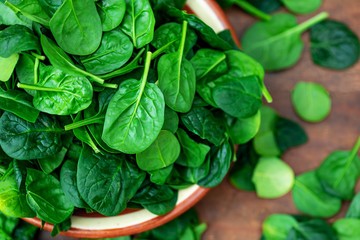 Fresh baby spinach leaves in a bowl on rustic wooden background, top view..