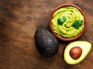 Avocado with guacamole sauce on a dark wood background. Half and whole avocadoes close up. Top view. Copy space.