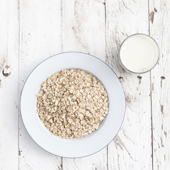 Oatmeal, rolled oats on a plate with glass of milk on white wooden table. Porridge oats, used in granola or muesli. Copyspace, flat lay.