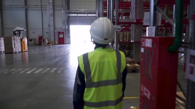 female warehouse worker with helmet and safety vest. Clip. Young female in protective uniform, helmet and eyeglasses holding walkie-talkie while working at plant