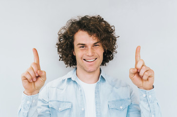 Portrait of curly hair amazed handsome man has happy expression, indicate index fingers up, good...