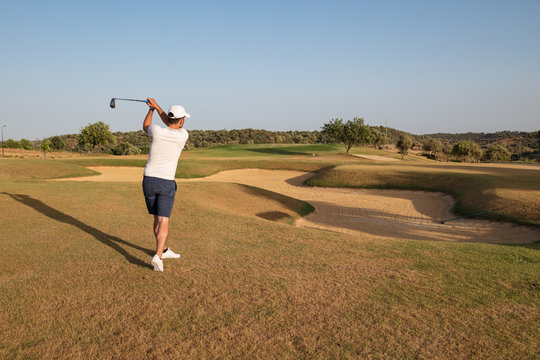 Golf player swinging ball over sand bunker