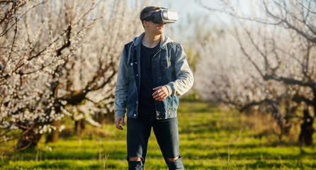 Young the guy of virtual reality glasses walk goes on the blossoming garden. Outdoor.