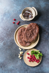 Ingredients for homemade sweet dessert chocolate pizza. Cocoa flat bread, different chocolates, raspberries, mint, jug of cream served on ceramic plates over blue texture background. Top view, space.