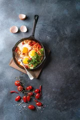 Keuken spatwand met foto Traditional Israeli Cuisine dishes Shakshuka. Fried egg with vegetables tomatoes and paprika in cast-iron pan on wooden board with coriander herbs over blue texture background. Top view, space. © Natasha Breen