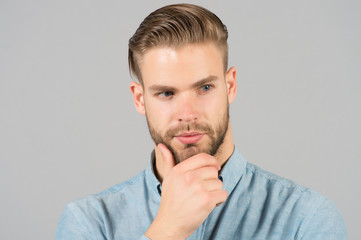 Obraz premium Macho with stylish hair touch beard with hand. Bearded man with healthy young skin. Guy with unshaven face and mustache. Beard grooming and hair care in barbershop. Skincare and mens beauty concept