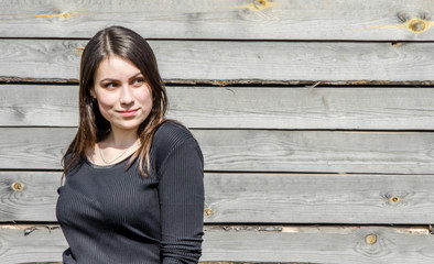 Portrait of a beautiful young brunette girl against a wall background of coarse-hewn gray boards.