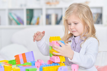 Cute little girl sitting at table and collecting colorful plasti