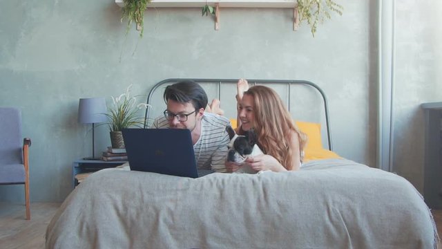 Happy young couple with french dog with laptop at home. Slow motion