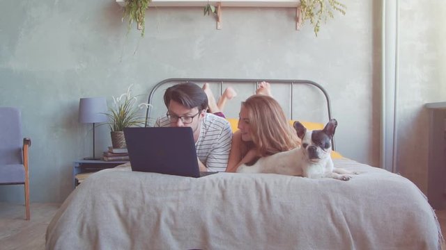 Happy young couple with french dog with laptop at home. Slow motion