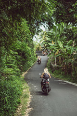 back view of girls riding motorbikes on road between tropical plants
