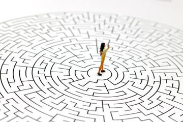 Miniature people: Businesswoman standing on center of maze. Concepts of finding a solution, problem solving and challenge.