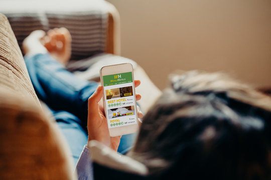 Woman Using A Mobile Phone To Search Hotel For Vacation While Rest On A Sofa At Home.