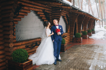 Stylish newlyweds embrace near a wooden cottage. Winter wedding. Snow love of the bride and groom.