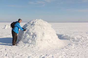 Fototapeta na wymiar Man building an igloo on a snowy reservoir in winter, Novosibirsk, Russia