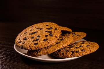 Plate with chocolate chip cookies on a dark wooden table