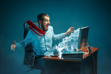 Young stressed handsome businessman working at desk in modern office shouting at laptop screen and being angry about spam