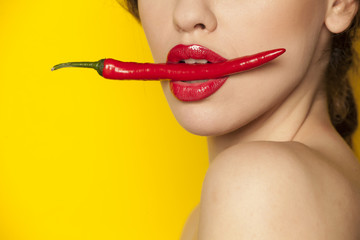 Young sexy woman holding a chili with her lips on yellow background