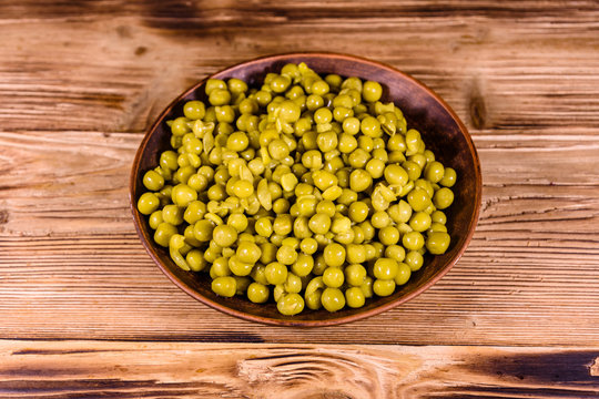 Ceramic plate with canned green pea on wooden table