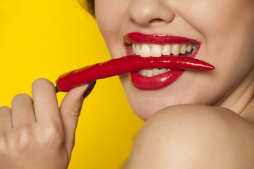 Young sexy woman holding a chili with her teeth on white background